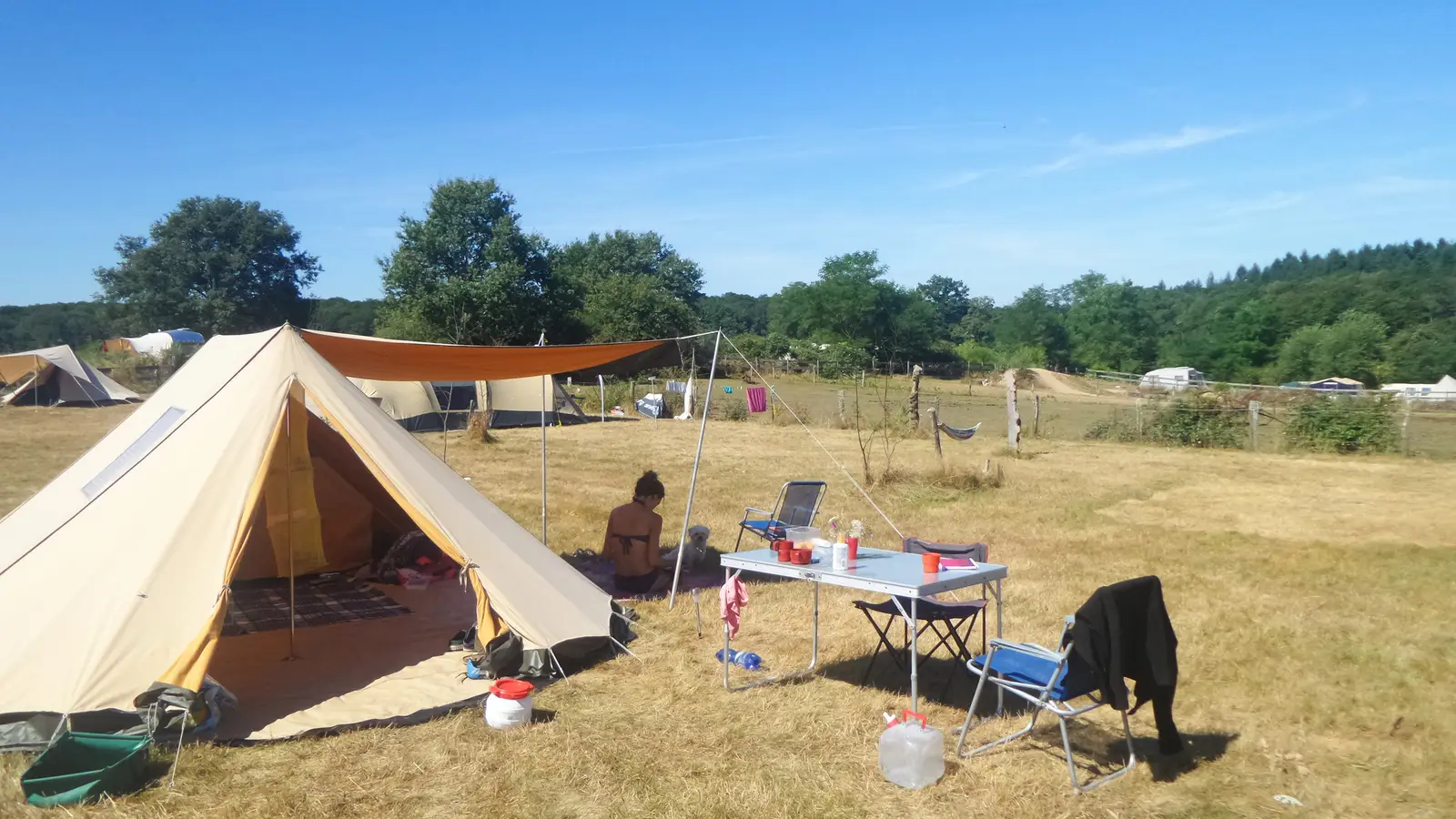 Kampeerders in de schaduw van hun luifel op een zonnig veld