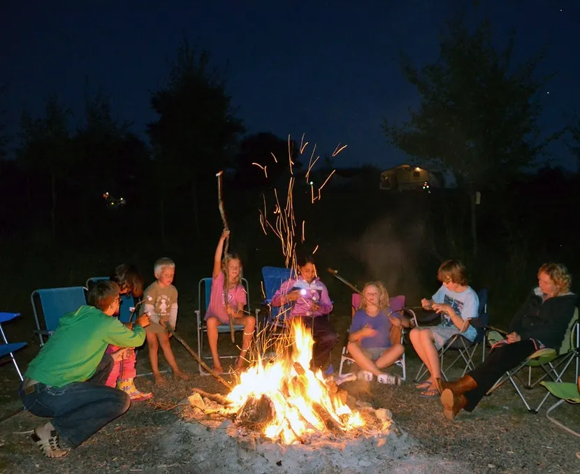 een groep zit rond een kampvuur op een donkere camping