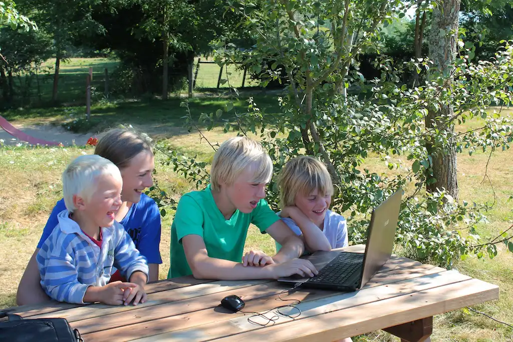 vier kinderen hebben plezier achter een laptop aan een picknicktafel